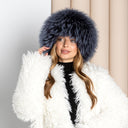 A woman wearing a white fur coat and a black and white striped shirt, with long blonde hair, is posing for a photograph.