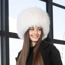 A woman with long brown hair wearing a white fur hat and smiling at the camera.