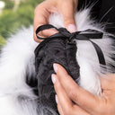 A person's hands holding a black quilted bag with a black ribbon tied around it.