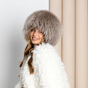 A woman wearing a white fur hat and a white fur coat is smiling at the camera.