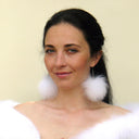 May include: A woman with long dark hair is wearing white fur earrings. She is wearing a white fur shawl.