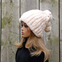 May include: A cream-colored faux fur beanie with a fluffy pom-pom on top. The beanie is ribbed and has a slouchy fit.